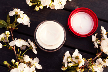 Tubes with creams on black ooden background with white flowers. View from above.