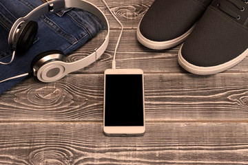 Denim pants, headphones, smartphone, sports shoes on wooden background.  recreation, sports. healthy lifestyle.