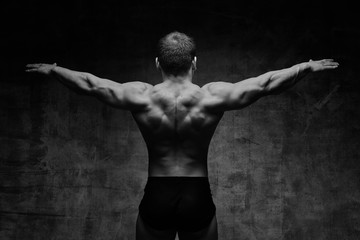 Fototapeta na wymiar Sexy bodybuilder man posing from the back on dark background. Handsome pumped male body isolated with free space for advertising