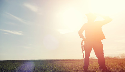 A man cowboy hat and a loso in the field. American farmer in a field wearing a jeans hat and with a...