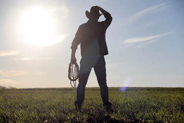 A man cowboy hat and a loso in the field. American farmer in a field wearing a jeans hat and with a...