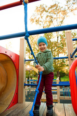 Cute 3 year old boy excitedly plays on a yellow playground slide.