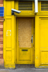 Bright yellow entrance supervised by a video camera. Entry clogged with plywood. The yellow door is...