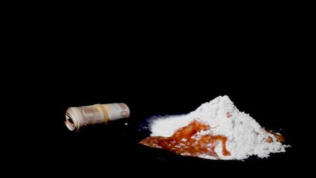 Close-up of a pile of white cocaine powder with blood in it beside a rolled up wad of money