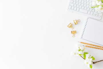 Flat lay blogger or freelancer workspace with a notebook, keyboard and white spring flowers on a white table
