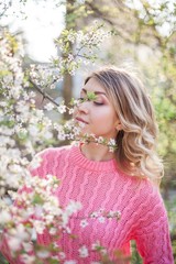 Spring portrait of a young blonde near a flowering tree. Happy young woman.