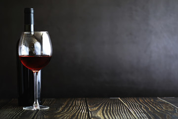A glass of red dry wine on the table. Dark bottle and glass of wine.