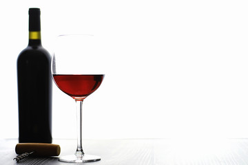 A glass of red dry wine on the table. Dark bottle and glass of wine.