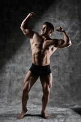 Fototapeta na wymiar Sexy bodybuilder man posing in full growth on dark background in black shorts. Handsome pumped male body isolated with free space for advertising
