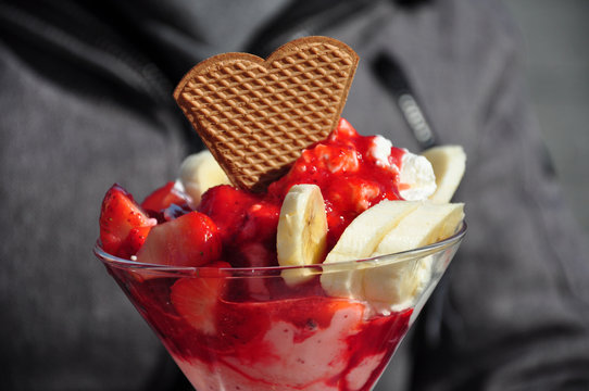 Der Erdbeereisbecher mit frischen Erdbeeren, Bananescheiben, Erdbeersoße und einer Herzwaffel. Leckeres Erdbeereis essen in der Eisdiele.