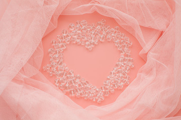 Flat lay in a fashionable frame with beads of Crystal heart tulle on a pink background with a copy...