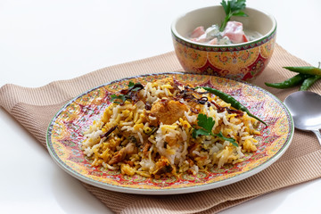 Halal Indian chicken Biryani served with yogurt tomato raita over white background. Selective focus.