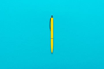 minimalist flat lay photo of yellow ballpoint pen over turquoise blue background