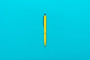 minimalist flat lay photo of yellow ballpoint pen over turquoise blue background