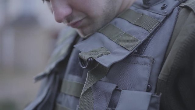 Unrecognizable young soldier putting on his light bulletproof vest close up. The man preparing for the war. Military and special forces equipment