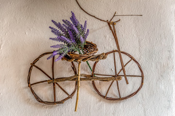 Purple wildflower on small bicycle ornament handmade using thin tree branches hanging on an old wall