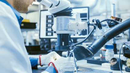 Close-Up Shot of an Electronics Factory Worker in White Work Coat Soldering a Printed Circuit Board Through a Digital Microscope. High Tech Factory Facility.