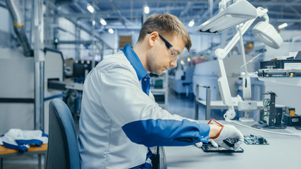 Young Man in Blue and White Work Coat is Using Plier to Assemble Printed Circuit Board for...