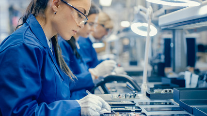 Female Electronics Factory Workers in Blue Work Coat and Protective Glasses Assembling Printed...