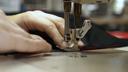 A seamstress in a seamstress factory (at home) sews clothes from fabric materials. Using a sewing machine in slow motion. Concept of: Factory, Work, Labor, Cloth, People, Macro, Clothes.