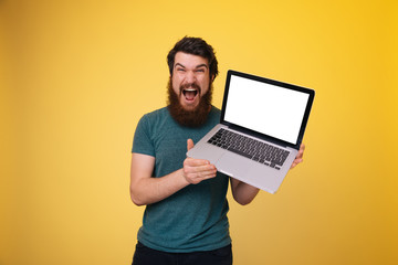 Bearded guy , excited showing a laptop in his hands over yellow isolated background