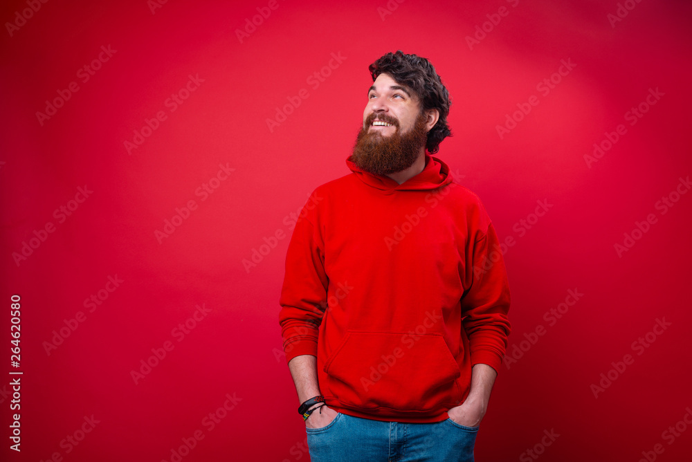 Wall mural Photo of a handsome cheerful bearded guy with hands in pockets and looking up away