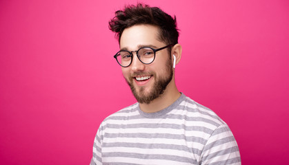 Photo of smiling man wearing glasses, and aipods, lookinf at camera over pink background