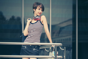 Happy young fashion woman with handbag leaning on railing