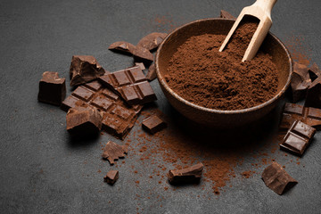 Dark Chocolate chunks and cocoa powder in wooden scoop on dark concrete background