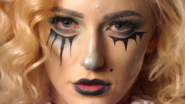 Make-up for Halloween. Slow motion. Halloween face art. Portrait of a beautiful woman looking at the camera, makeup the bride's corpse, black accents under eyes and lips, green background.