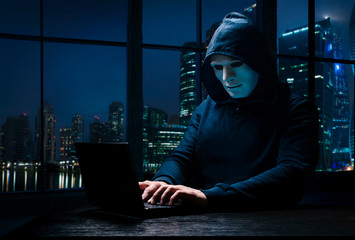 Masked hacker with a laptop. Organizing Massive Data Breach Attack