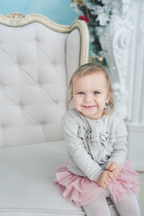 Fototapeta premium cute little child sitting in chair near Christmas tree. Happy new year. Portrait little girl. Christmas concept.