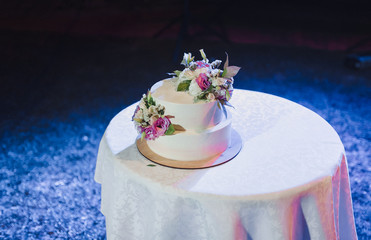 A beautiful wedding cake, decorated with roses, stands on a round table in a restaurant. Wedding party. Tasty pie.
