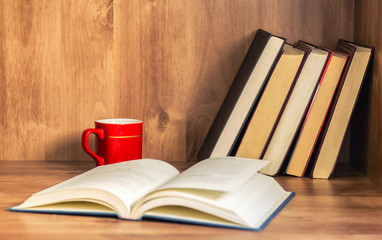 Pile of closed books and open book with cup of coffee on wooden background.