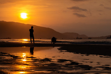 Silhouettes of people on the background of a golden dawn on the beach of Sanya, Hainan Island, China