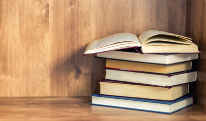 Pile of closed books with open book on wooden background.