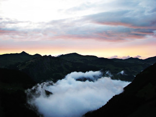 Fog and white smoke clouds in the Alps mountains at sunset.