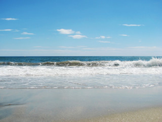 Waves tide near the shore on a sandy beach and blue sky.