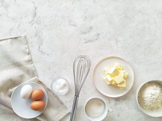 Ingredients for the cake: eggs, flour, sugar, butter, baking powder. Top view on light background.