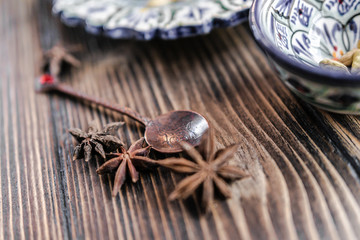 Authentic middle east style bronze spoon with a cinnamon on the wooden desk with a colourful eastern bowl and a plate on the black background. Isolated. Shallow depth of field. Horizontal orientation.
