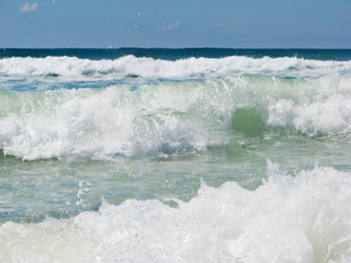 White waves crashing and splashing with foam near the shore in the sun on the ocean for the background.