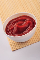 Small one bowl of red tomato sauce ketchup isolated on gray background on bamboo stand