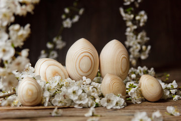 wooden easter eggs among flowering cherry branches on a rustic table. symbolic composition of the spring holiday for a gift card. copy space. close up. petals of white flowers. the rebirth of nature