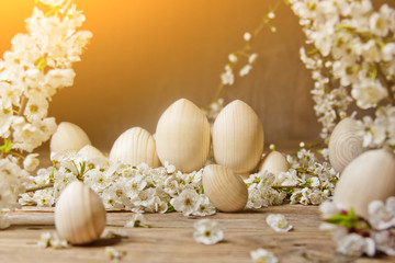 wooden easter eggs among flowering cherry branches on a rustic table. symbolic composition of the spring holiday for a gift card. copy space. close up. petals of white flowers. the rebirth of nature