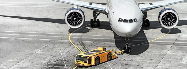 Fototapeten Flugzeug auf der Landebahn des Flughafens mit Pushback-Traktor, der am Bugfahrwerk des Flugzeugs befestigt ist © vaalaa