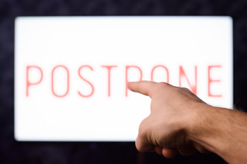 Male`s hand pointing to a screen with inscription POSTPONE in order to show reason of many problems. People shouldn't postpone things and actions