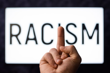 European male showing middle finger to inscription Racism on a screen in order to show his attitude towards racists