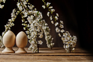 Obraz na płótnie Canvas A couple of wooden Easter eggs among flowering cherry branches on a rustic table. symbolic composition of the spring holiday for a gift card. copy space. close up. white petals. the rebirth of nature