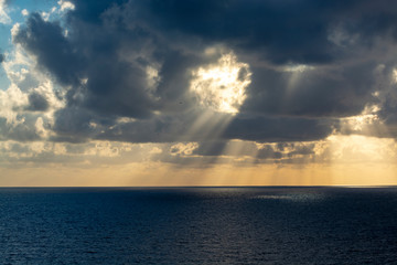 Dramatic sunset over sea water with gray clouds and sun lights