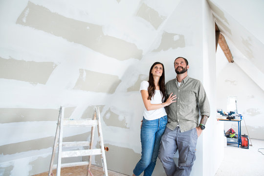 Confident couple standing in attic to be renovated looking up